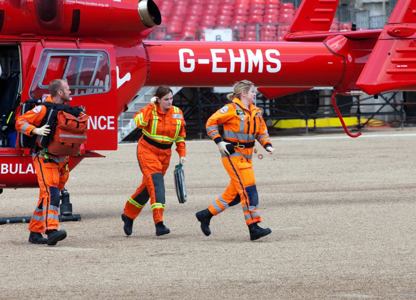 Air ambulance crew in orange flight suits walking away from a red helicopter during an emergency response