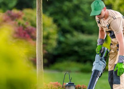 Gardener using a leaf blower to clear debris in a landscaped garden